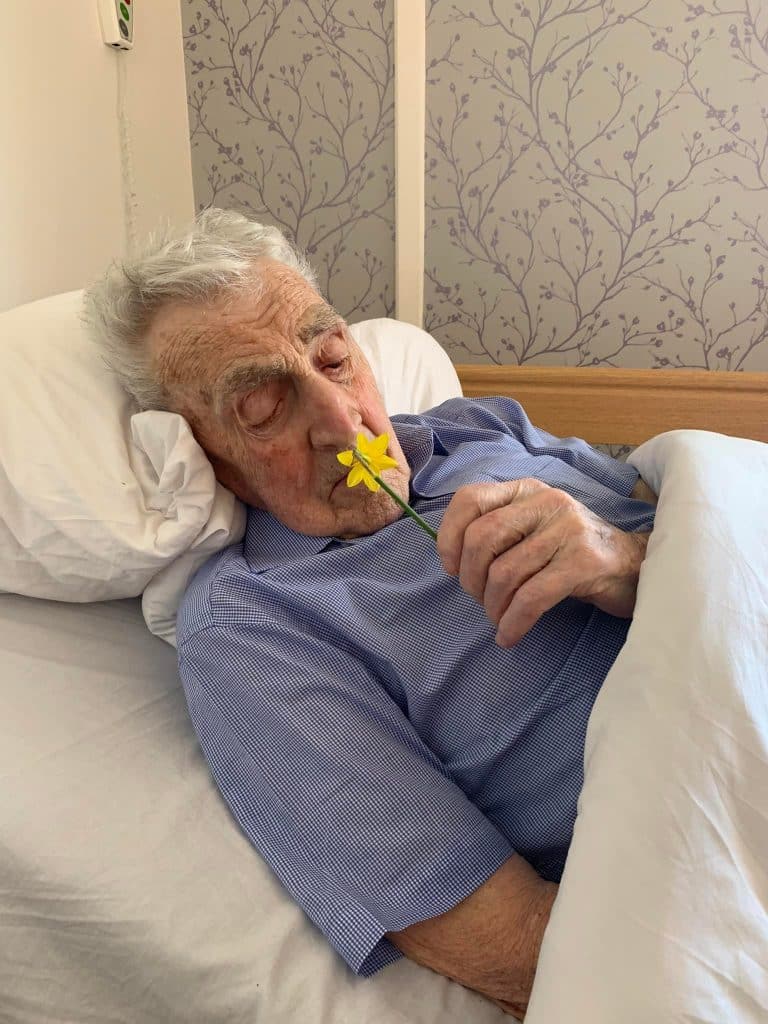 gentleman resident in bed smelling daffodil